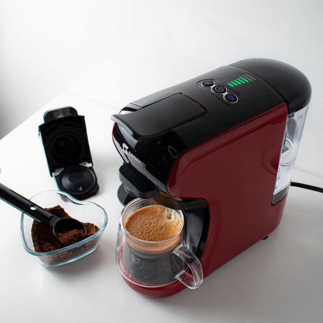 Red and black coffee machine with a glass carafe on a white surface, surrounded by coffee grounds and a scoop.
