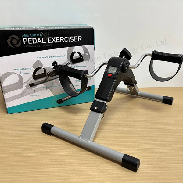 Pedal exerciser with digital display on a wooden surface, next to its packaging box.
