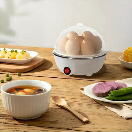 A white electric egg cooker with a clear lid sits on a wooden table, steaming several eggs. Surrounding it are bowls of soup, sliced purple sweet potato, green beans, and corn on a plate, with a wooden spoon in the foreground.