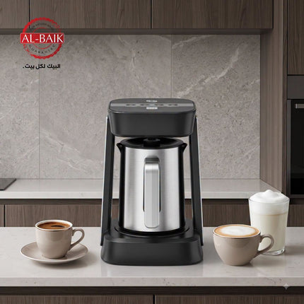 A countertop coffee maker with a stainless steel carafe and black base stands on a light stone kitchen counter. Two cups, one with coffee and one with milk, are placed on either side.