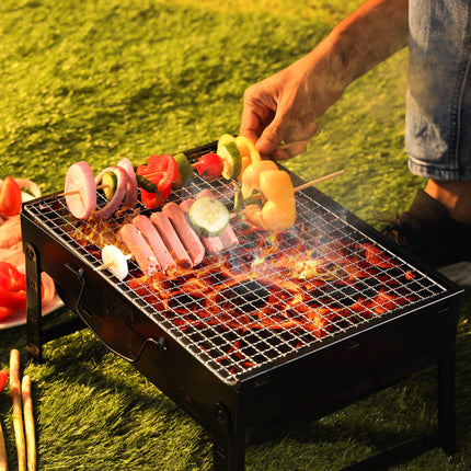 Person grilling skewers on a portable barbecue grill outdoors.