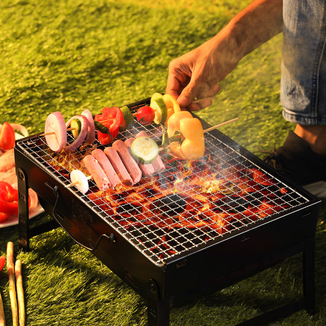 Person grilling skewers on a portable barbecue grill outdoors.